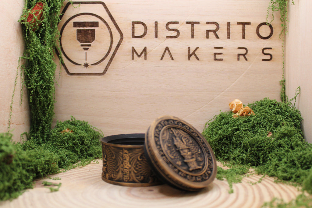Cajita cilíndrica del castillo en dorado con la tapa apoyada, sobre el fondo del taller — Distrito Makers