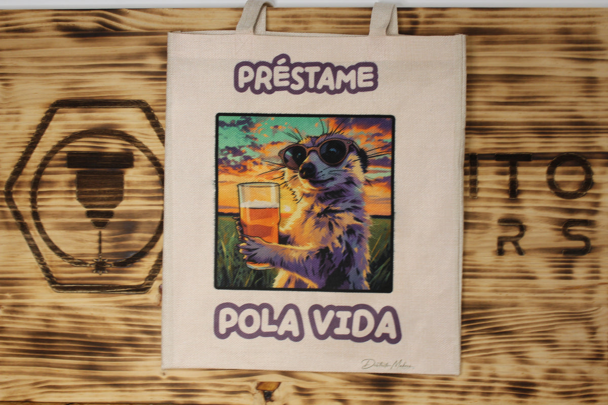 Tote bag de tela símil lino con el lema en asturiano «Préstame pola vida» y una suricata con gafas de sol tomando una caña al atardecer