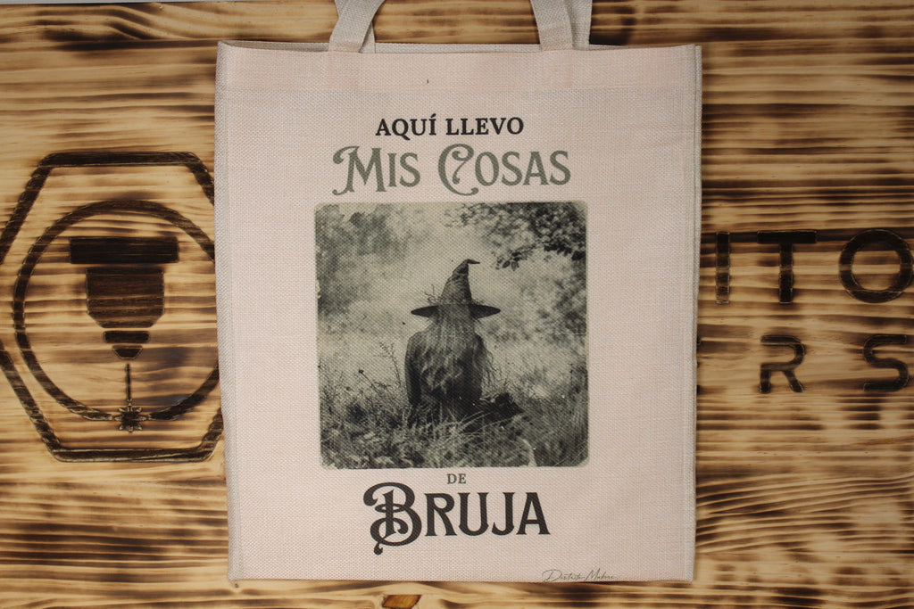 Tote bag de tela símil lino con el lema «Aquí llevo mis cosas de bruja» y la foto en sepia de un cuervo con sombrero de bruja entre la hierba