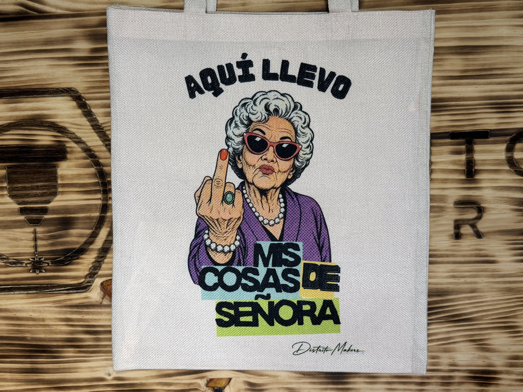 Tote bag de tela símil lino con el lema «Aquí llevo mis cosas de señora» y la ilustración de una señora con gafas de sol rojas haciendo una peineta