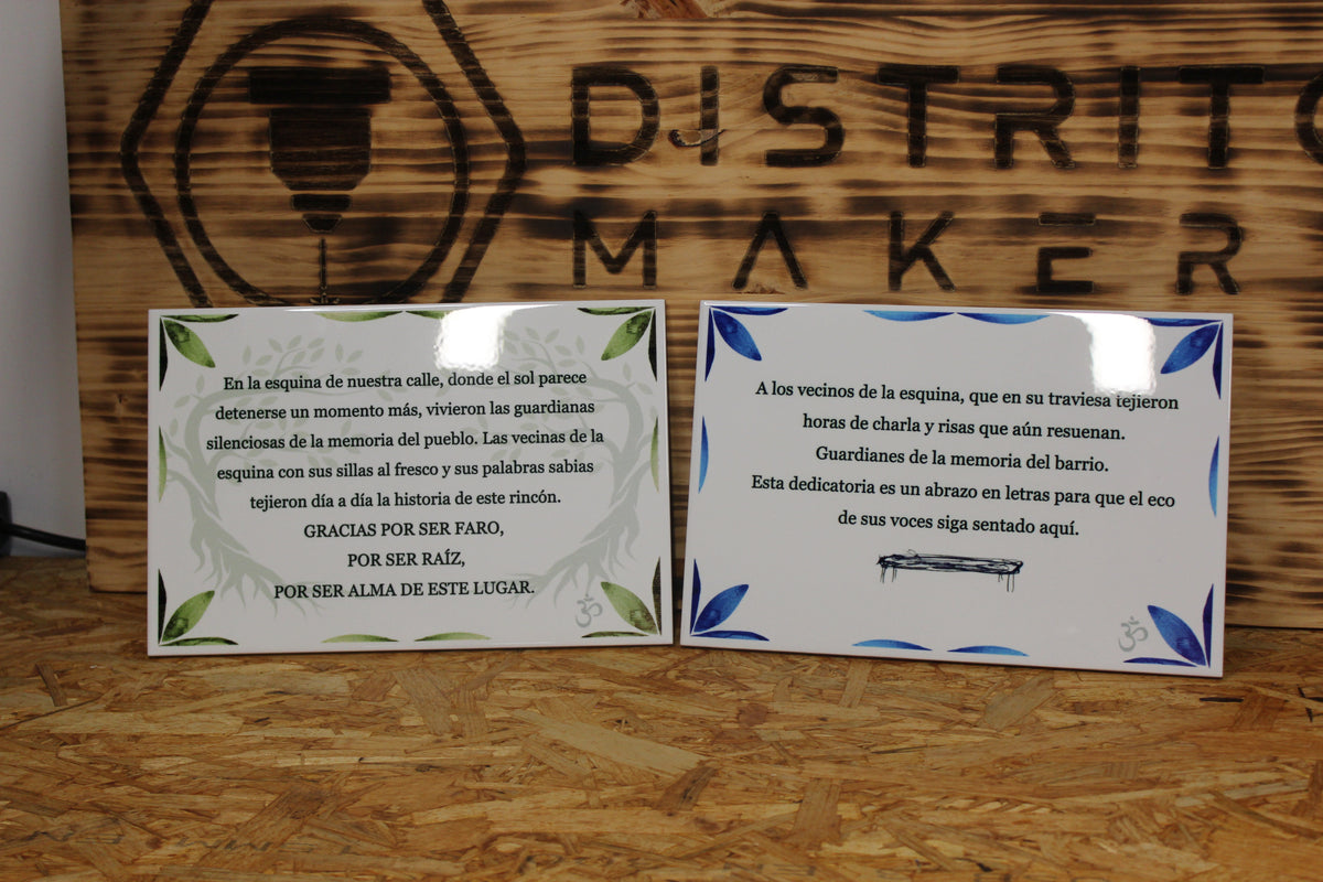 Dos azulejos personalizados de 20 × 30 cm con dedicatorias a los vecinos de la esquina, uno con cenefa de hojas verdes y otro con cenefa de hojas azules, delante del logo de Distrito Makers grabado en madera