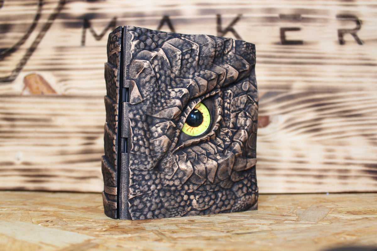 Caja secreta El Ojo del Cuélebre en dorado oscuro, con un ojo de dragón amarillo