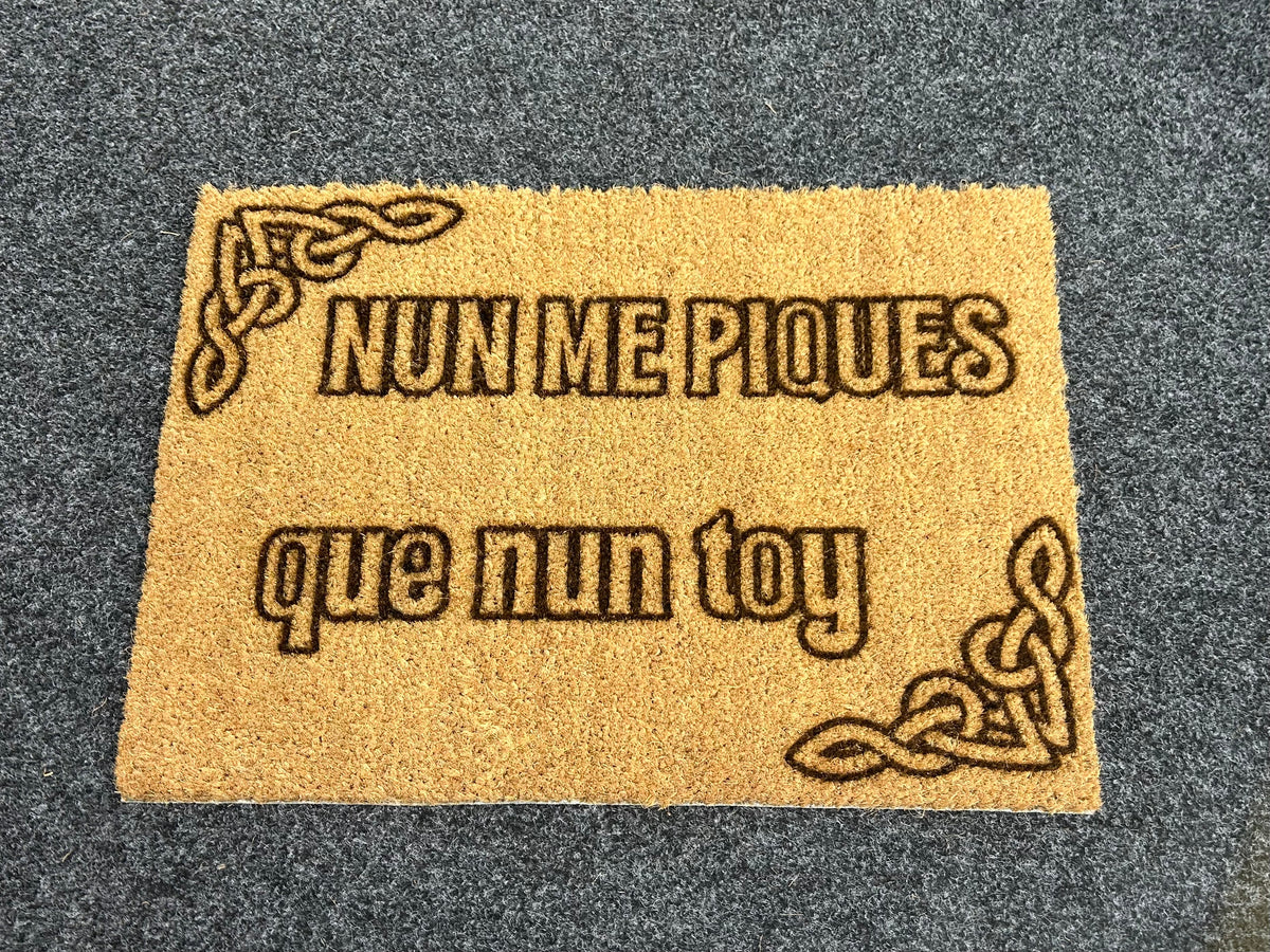 Felpudo de fibra de coco grabado con la frase en asturiano «Nun me piques, que nun toy» y dos nudos celtas en las esquinas